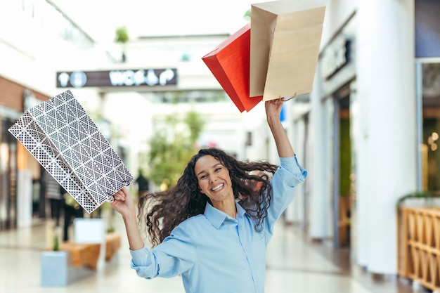 Felice shopper donna che guarda l'obbiettivo e sorridente donna ispanica con capelli ricci che ballano e saltano