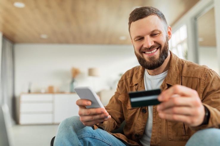 Foto felice shopping maschile utilizzando smartphone e carta di credito seduti all'interno