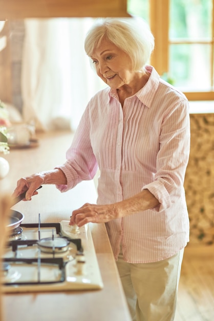 Felice signora anziana in piedi in cucina e prepara il cibo