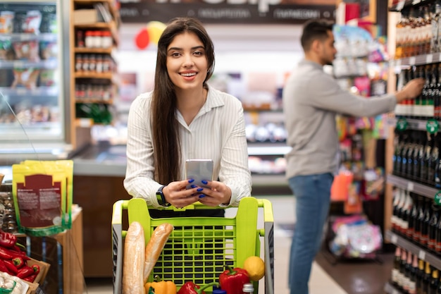 Felice signora araba utilizzando il telefono in un negozio di alimentari