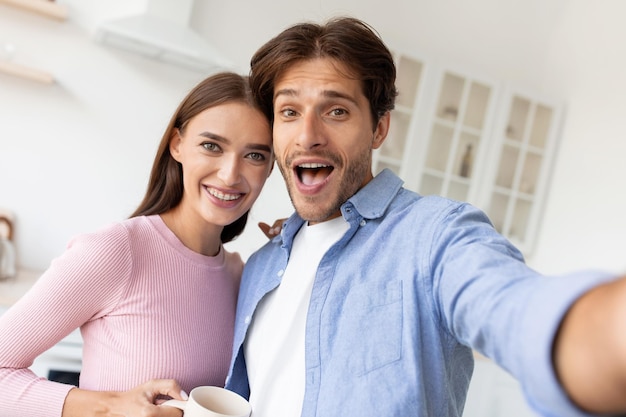 Felice soddisfatta femmina europea millenaria con una tazza di bevanda e un uomo con la bocca aperta che guarda la webcam