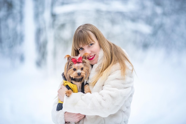 Felice sorridente fiducioso giovane donna bianca bel viso con piccolo cucciolo Yorkshire Terrier nella foresta innevata