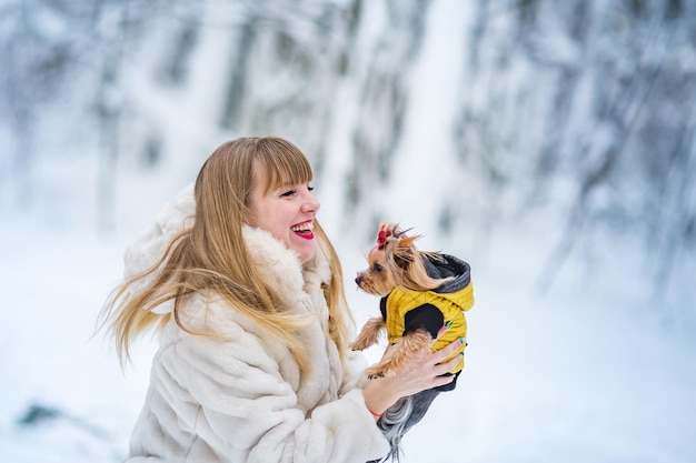 Felice sorridente fiducioso giovane donna bianca bel viso con piccolo cucciolo Yorkshire Terrier nella foresta innevata