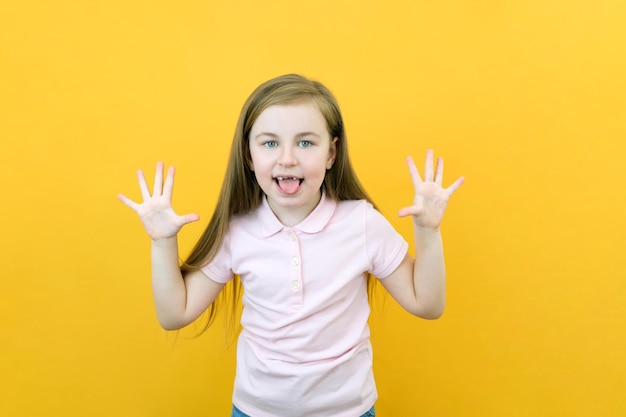 Felice sorriso positivo ragazza che mostra dieci dita che si conficca fuori la lingua isolata su sfondo di colore giallo