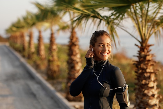 Felice sportiva che distoglie lo sguardo stando in piedi nella natura e ascoltando musica con gli auricolari