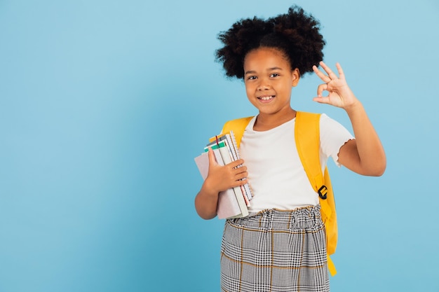 Felice studentessa afroamericana che punta fresco su sfondo blu torna al concetto di scuola