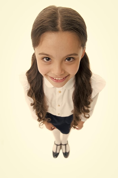 Felice studentessa con i capelli lunghi isolata on white Bambina sorridente in uniforme scolastica vista dall'alto Servizio di parrucchiere per piccola ragazza Bambino carino con un sorriso adorabile Acconciatura perfetta Salone di bellezza