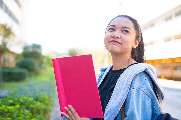 Felice studentessa tenere libro e zaino a scuola, ragazza asiatica.
