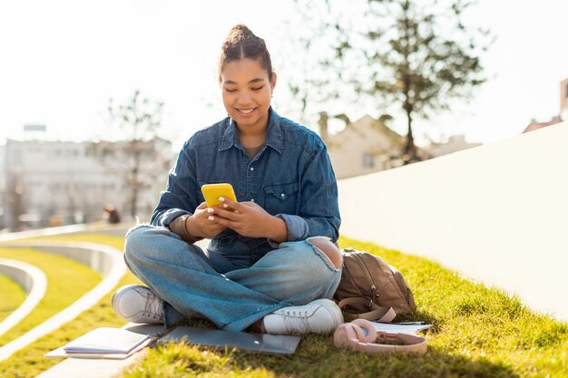 Felice studentessa universitaria che utilizza il cellulare e invia messaggi di testo online seduti all'aperto nello spazio libero del parco urbano