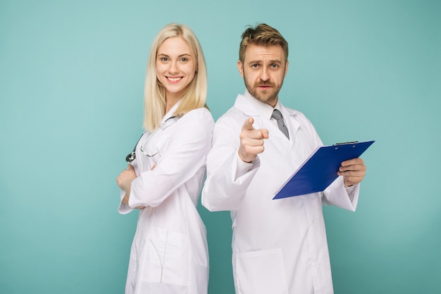 Felice team medico di medici, uomo che punta alla donna anteriore e sorridente, isolato su uno spazio blu