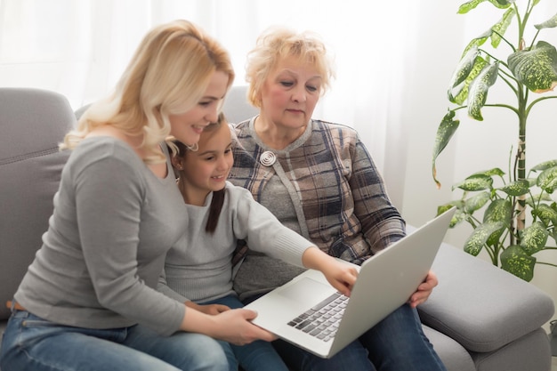 Felice tre generazioni di donne si siedono rilassarsi sul divano ridere guardando video divertenti sul computer portatile, sorridenti femmine positive nonna, madre e figlia si divertono a riposare sul divano godersi film sul computer