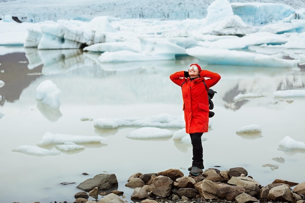Felice turista femminile in giacca rossa e occhiali si trova vicino a un ghiacciaio. Laguna glaciale di Jokulsarlon