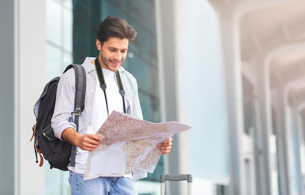 Felice turista giovane in piedi vicino all'aeroporto con la mappa in mano