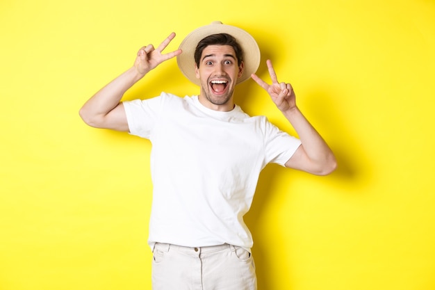 Felice turista maschio in posa per una foto con segni di pace, sorridendo eccitato, in piedi contro il muro giallo