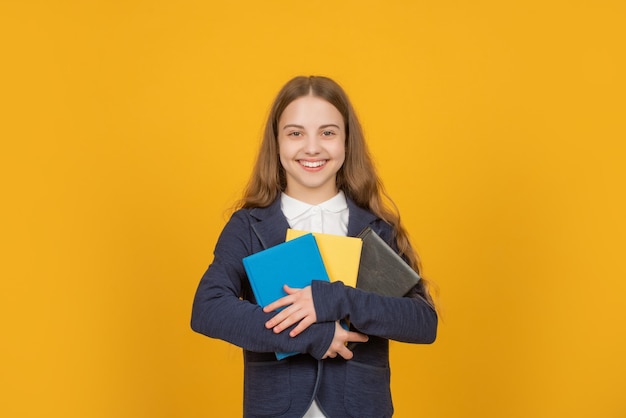 Felice tween ragazza tenere la cartella di lavoro della scuola su sfondo giallo, scuola.