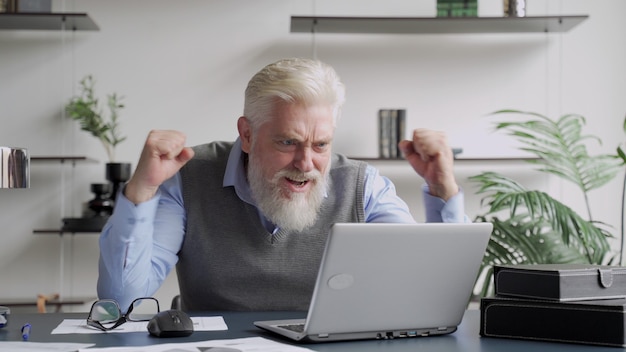 Felice un uomo anziano con la barba grigia ha completato il compito e trionfante con le mani alzate