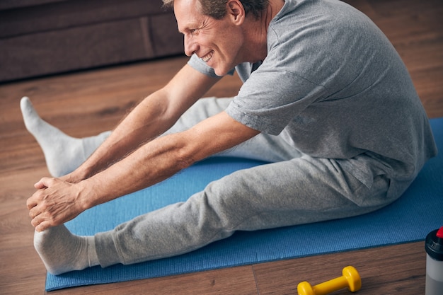 Felice uomo adulto gentile che sorride e usa il tappetino mentre fa sport a casa