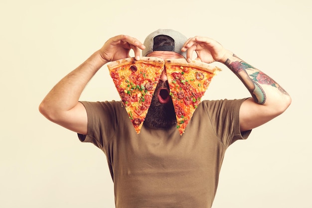 Felice uomo affamato che mangia pizza L'uomo barbuto tiene in mano due pezzi di pizza