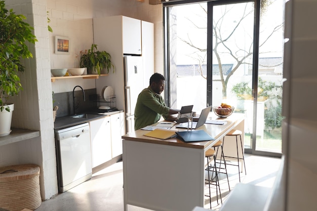 Felice uomo afroamericano seduto al tavolo in cucina utilizzando il computer portatile. Trascorrere del tempo di qualità a casa da solo.