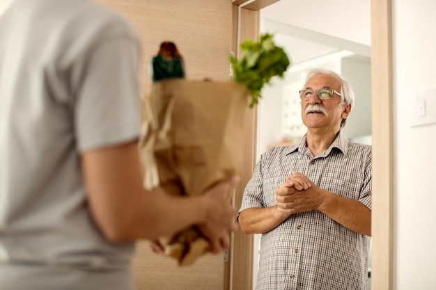 Felice uomo anziano che riceve la consegna di generi alimentari a casa