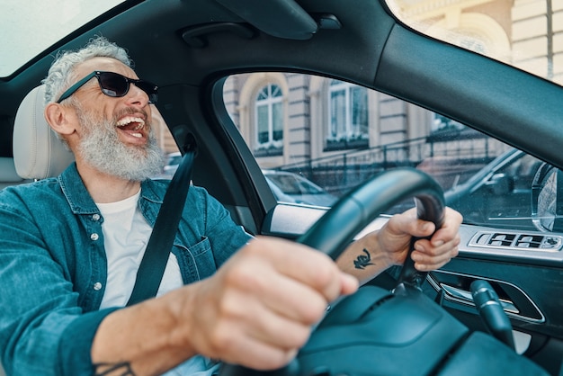 Felice uomo anziano in abbigliamento casual che si gode il giro in macchina e ride