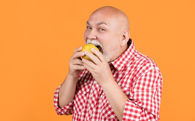 Felice uomo anziano morso mela su sfondo giallo