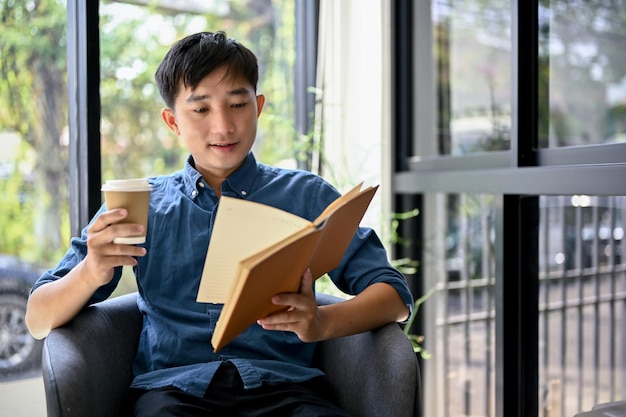 Felice uomo asiatico godendo con il suo caffè e leggendo un libro in una caffetteria