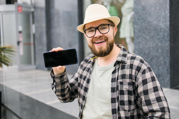 Felice uomo barbuto che mostra lo schermo vuoto dello smartphone su sfondo urbano spazio vuoto per la pubblicità