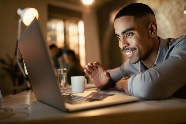 Felice uomo d'affari afroamericano che legge un'e-mail mentre lavora fino a tardi su un computer in ufficio