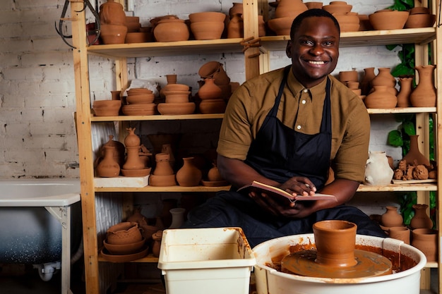 Felice uomo d'affari afroamericano potter proprietario maschio che fa scultura in argilla vaso tazza al banco di lavoro in officina studio creatività e mercante di porcellana creativa