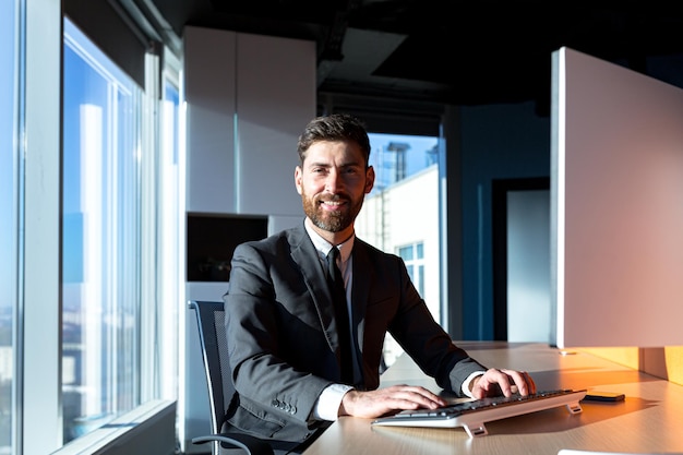 Felice uomo d'affari di successo con la barba che lavora al computer in un ufficio moderno sorridente e gioioso capo fiducioso