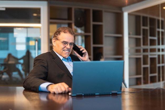 Felice uomo d'affari maturo utilizzando computer portatile e telefono cellulare in ufficio