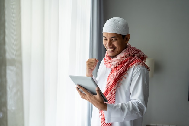 Felice uomo d'affari musulmano sorridente durante l'utilizzo di tablet pc vicino alla finestra