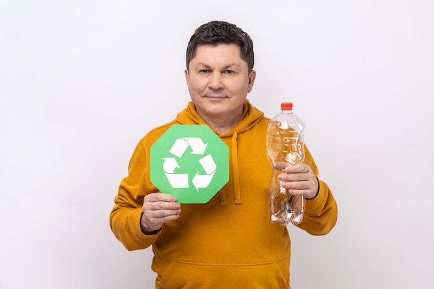 Felice uomo dai capelli scuri con un sorriso che tiene in mano una bottiglia di plastica vuota e un cartello verde di riciclaggio