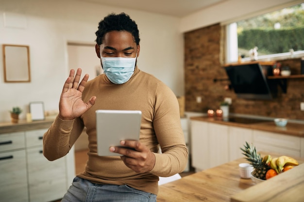 Felice uomo di colore che sventola durante la videochiamata sul touchpad a casa durante la pandemia COVID19