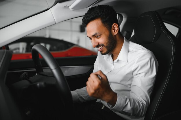 Felice uomo indiano che controlla le caratteristiche dell'auto presso lo showroom