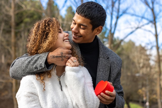 Felice uomo latino che fa un regalo alla sua ragazza Ragazzo che fa un regalo di San Valentino alla sua ragazza all'aperto