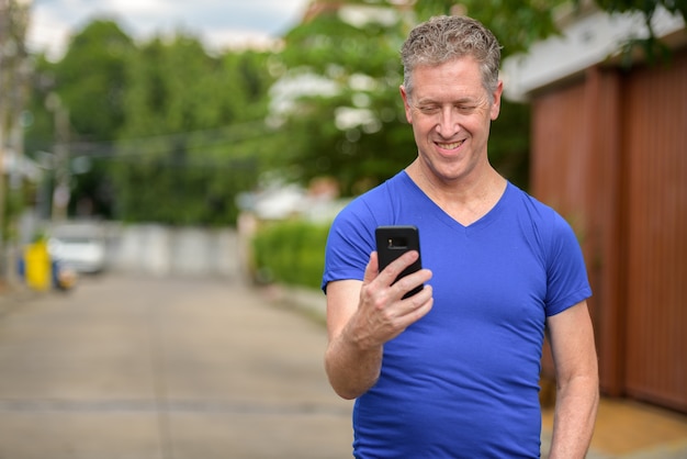 Felice uomo maturo utilizzando il telefono nelle strade all'aperto