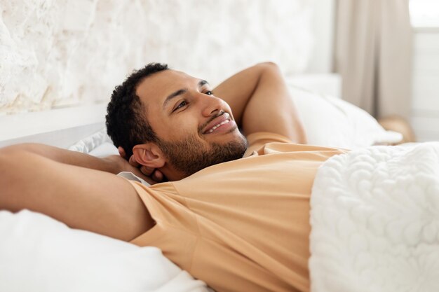 Felice uomo mediorientale rilassante sdraiato riposando in un'accogliente camera da letto