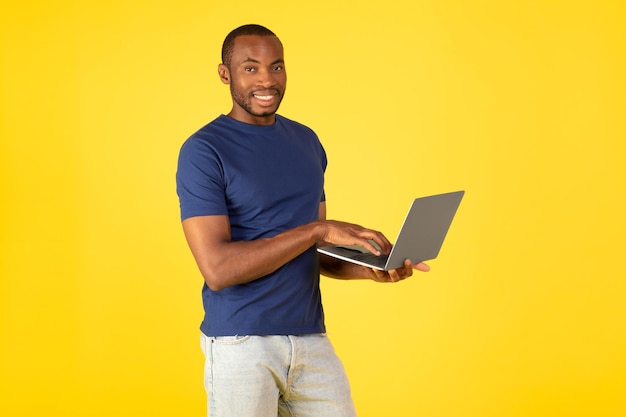 Felice uomo nero utilizzando laptop in posa su sfondo giallo