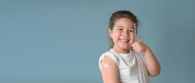 Felice vaccinata piccola ragazza asiatica che mostra il braccio con una benda di gesso dopo l'iniezione del vaccino Covid19