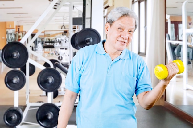 Felice vecchio esercizio con manubri nel centro della palestra