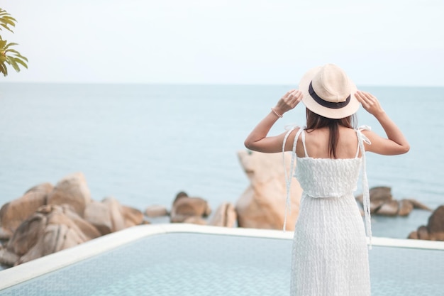 Felice viaggiatore donna in abito bianco e cappello godere di una splendida vista sul mare giovane donna in piedi in piscina Libertà rilassante vacanza vacanza e concetto di viaggio estivo