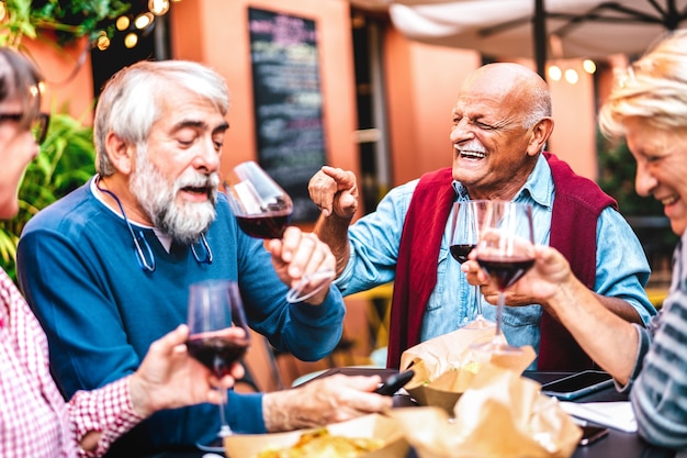 Felici amici in pensione che si divertono a bere vino rosso alla festa prima di cena