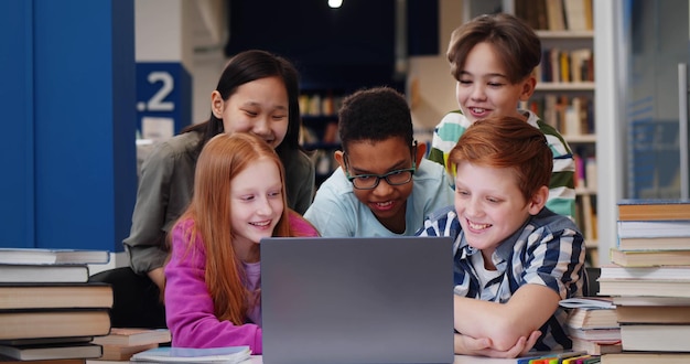 Felici compagni di classe multietnici che usano il computer insieme nella biblioteca scolastica