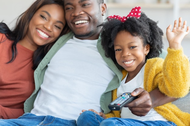 Felici giovani genitori neri e la loro piccola figlia che guardano la tv a casa