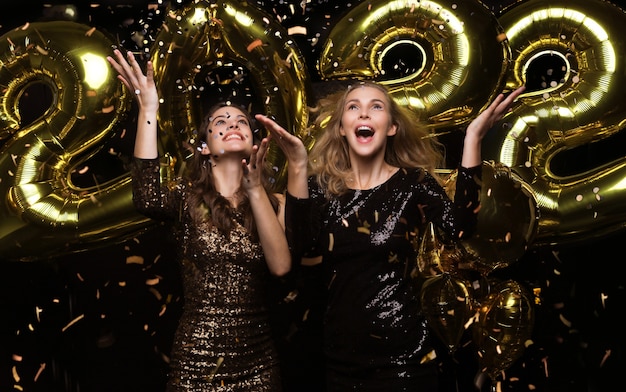 Felici ragazze bellissime in eleganti abiti da festa sexy con palloncini d'oro 2022, che si divertono alla festa di Natale o di Capodanno.