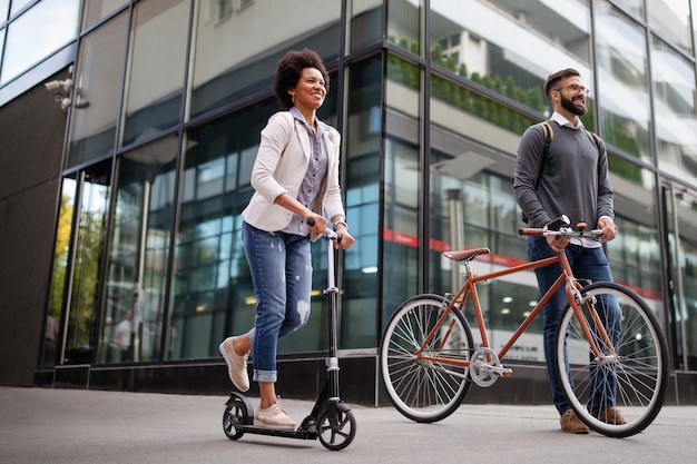 Felici uomini d'affari ecologici che vanno a lavorare con biciclette, scooter elettrici su strade urbane