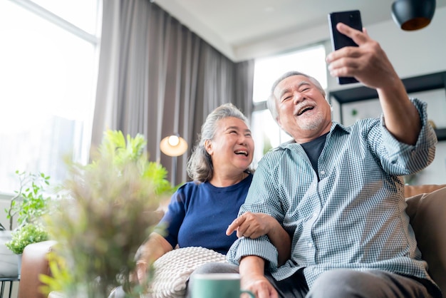 Felicità asiatica vecchia coppia pensionata senior gode di una videochiamata alla famiglia insieme sul divano in soggiorno a persone homeasiatiche usano la comunicazione dello smartphone al concetto di isolamento domestico della famiglia