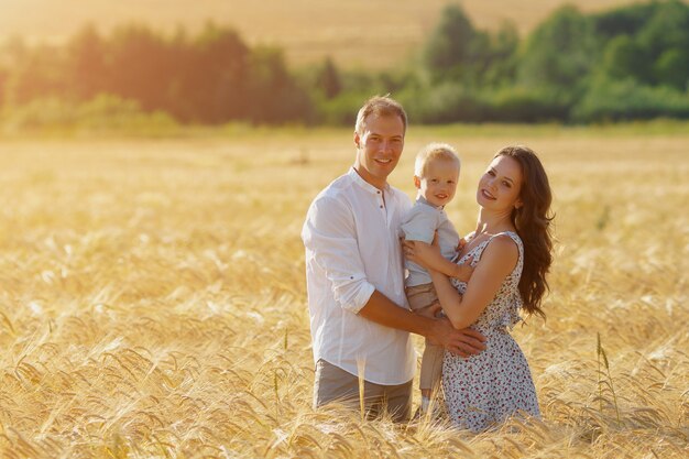 Felicità dei genitori, camminando sul campo con il bambino. Madre, padre e bambino svaghi insieme all'aperto. copyspace, luce solare